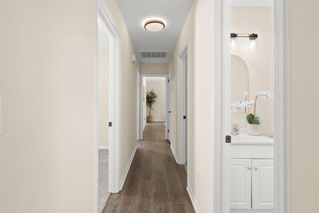 corridor with dark wood-style flooring, a sink, and baseboards