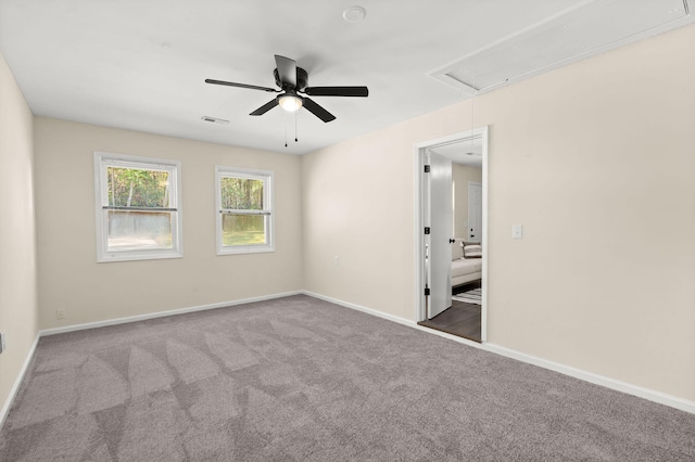 empty room featuring attic access, carpet floors, ceiling fan, and baseboards