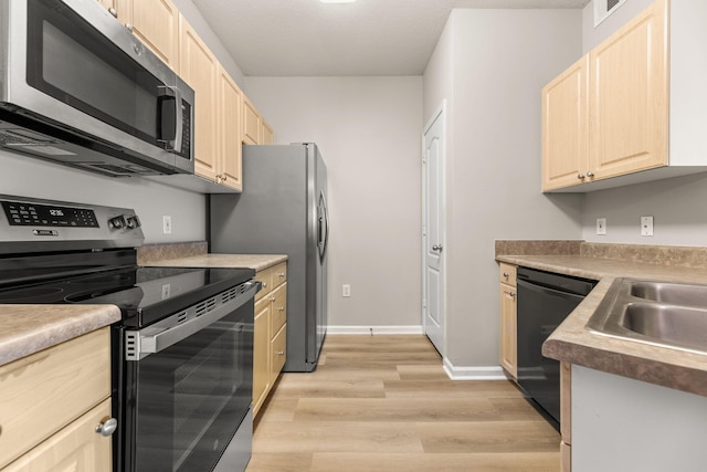 kitchen with appliances with stainless steel finishes, light brown cabinetry, sink, and light wood-type flooring