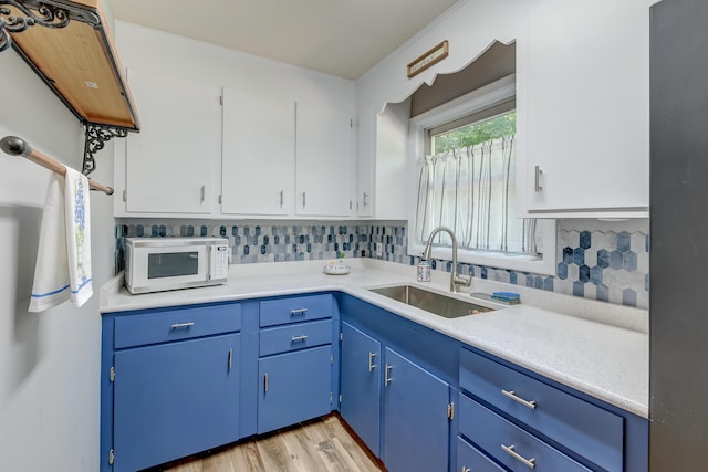 kitchen featuring a sink, white microwave, light countertops, tasteful backsplash, and blue cabinets