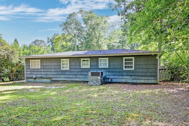rear view of house with central air condition unit, fence, and a lawn
