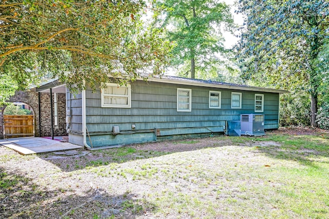 view of side of home with fence, central AC unit, and a lawn