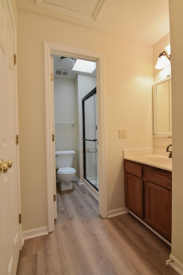 bathroom with wood-type flooring, a textured ceiling, a shower with shower door, toilet, and vanity