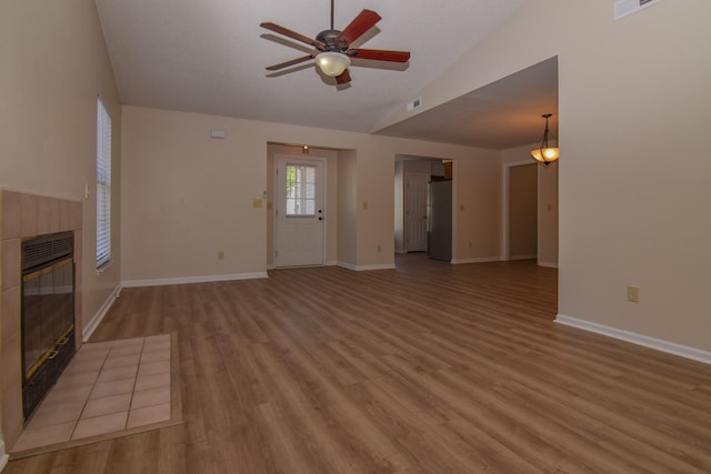 unfurnished living room featuring a tiled fireplace, vaulted ceiling, light hardwood / wood-style flooring, and ceiling fan