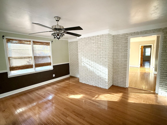 spare room featuring ceiling fan, hardwood / wood-style floors, brick wall, and ornamental molding