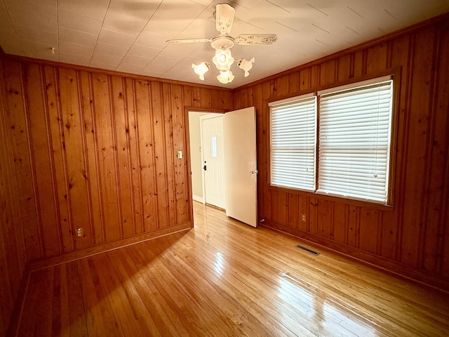 unfurnished room featuring light hardwood / wood-style flooring, ceiling fan, ornamental molding, and wood walls