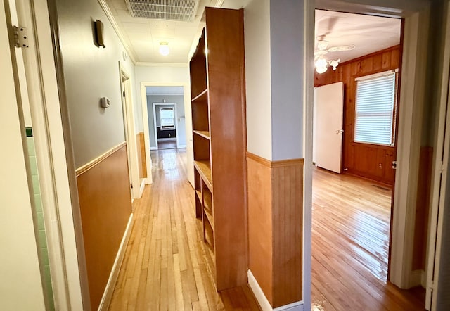 hall featuring light wood-type flooring, crown molding, wooden walls, and an inviting chandelier