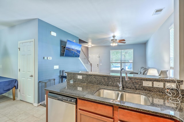 kitchen featuring a sink, dishwasher, dark stone counters, a ceiling fan, and visible vents