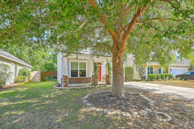 view of property hidden behind natural elements featuring curved driveway, fence, stone siding, and a front lawn