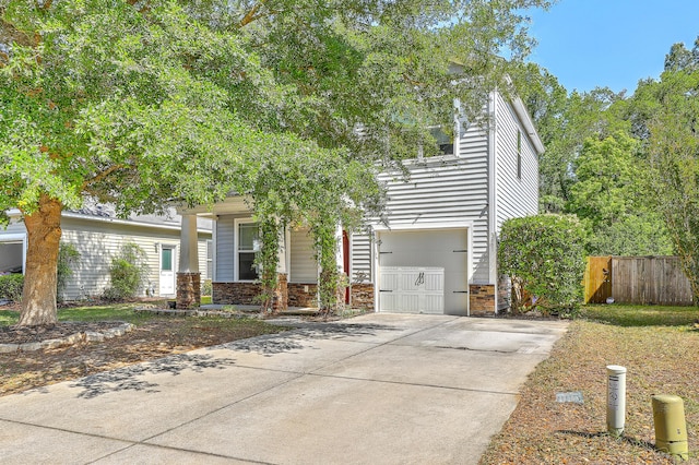 obstructed view of property with a garage, fence, stone siding, and concrete driveway