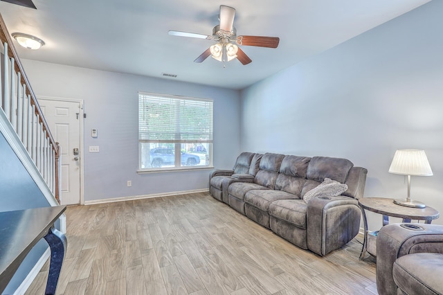 living room with visible vents, stairs, baseboards, a ceiling fan, and light wood-style flooring