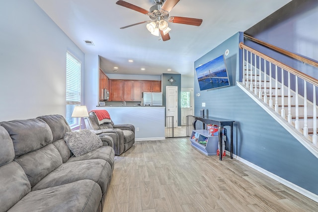 living room with a ceiling fan, visible vents, baseboards, light wood-style floors, and stairs