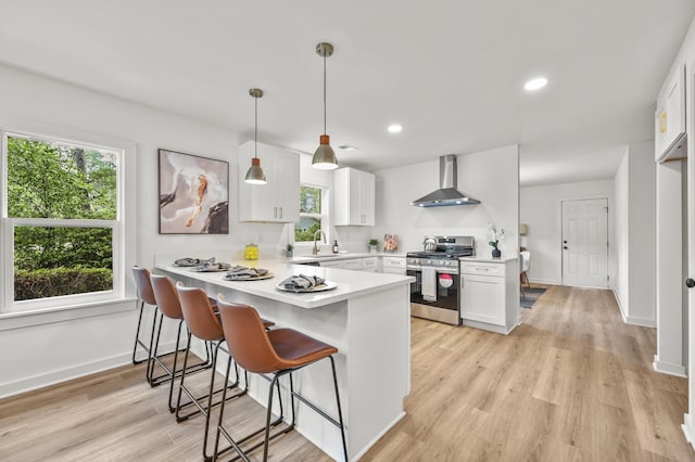 217 Quaker Rd, Saint George, SC 29477 - kitchen featuring wall chimney exhaust hood, gas range, a peninsula, white cabinets, and a kitchen breakfast bar