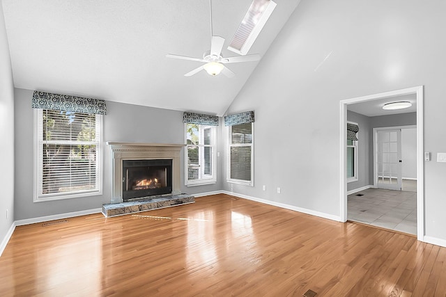 unfurnished living room featuring hardwood / wood-style floors, a skylight, high vaulted ceiling, and plenty of natural light