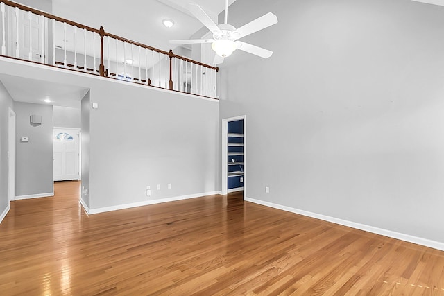 unfurnished living room with a towering ceiling, hardwood / wood-style flooring, and ceiling fan