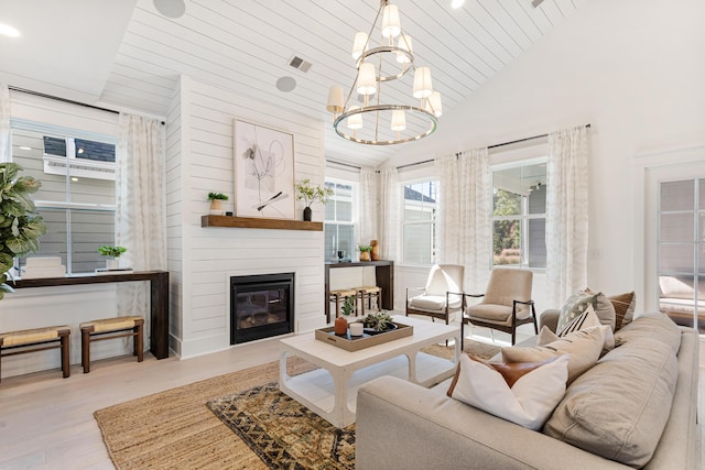 living area featuring visible vents, a glass covered fireplace, wood finished floors, high vaulted ceiling, and a chandelier