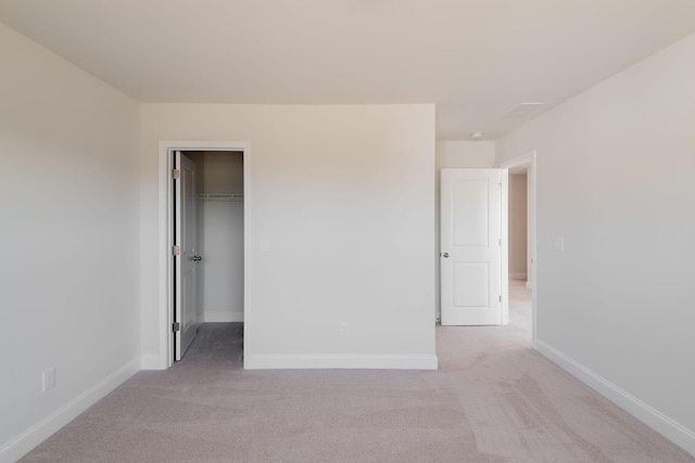unfurnished bedroom with baseboards, light carpet, and a walk in closet