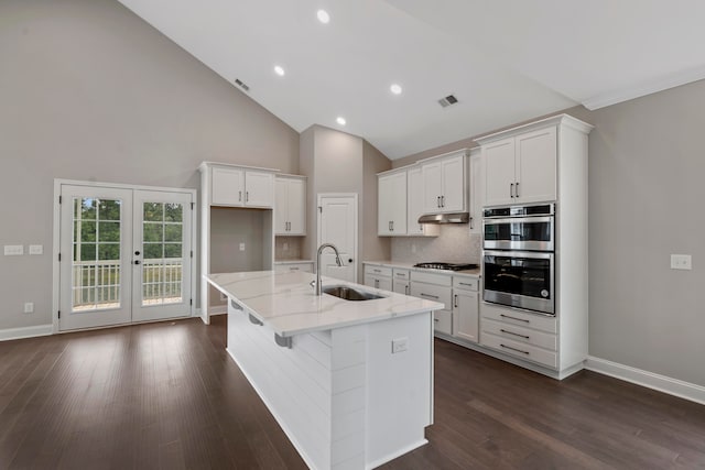 kitchen with light stone countertops, stainless steel appliances, sink, white cabinets, and an island with sink