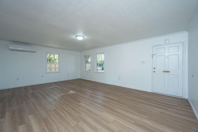 spare room with light hardwood / wood-style floors, ornamental molding, a textured ceiling, and a wall unit AC