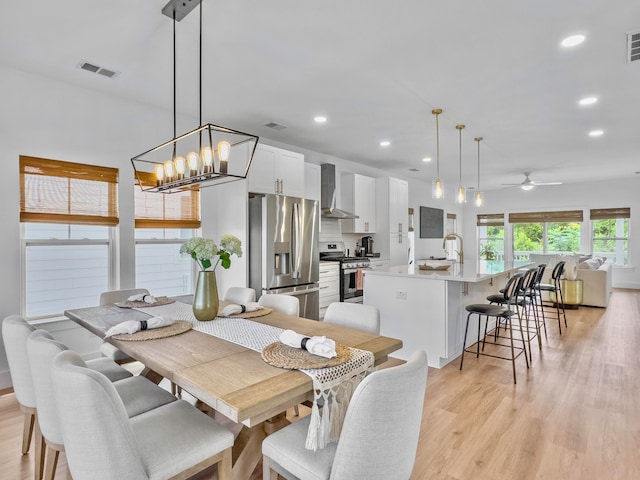 dining area with sink, ceiling fan with notable chandelier, and light wood-type flooring