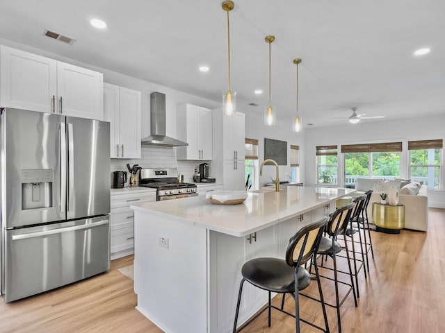 kitchen with a center island with sink, white cabinets, wall chimney range hood, appliances with stainless steel finishes, and a kitchen bar