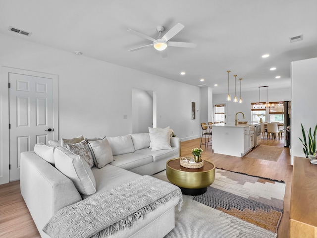 living room with ceiling fan with notable chandelier and light hardwood / wood-style floors