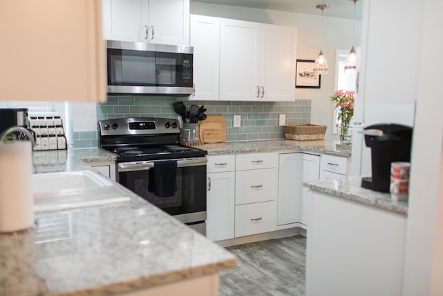 kitchen featuring pendant lighting, white cabinets, decorative backsplash, light wood-type flooring, and stainless steel appliances