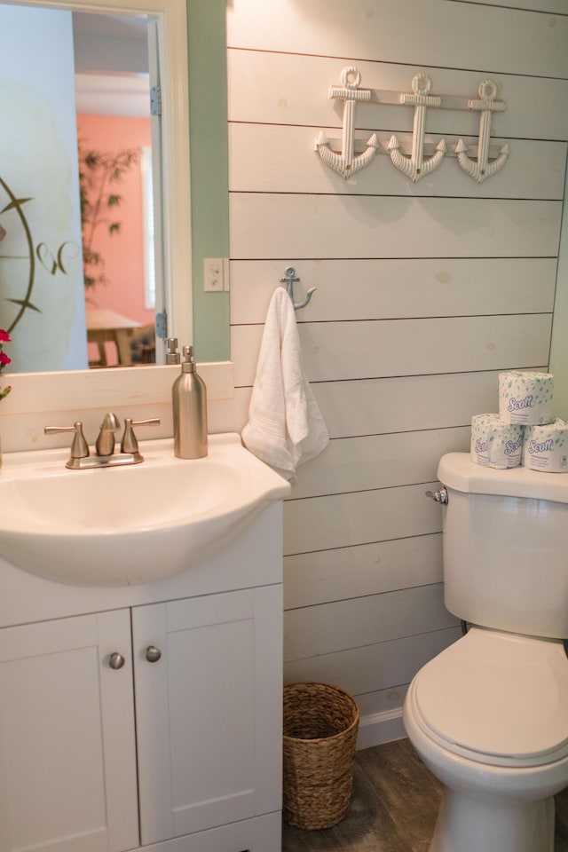 bathroom featuring vanity, wood walls, toilet, and wood-type flooring