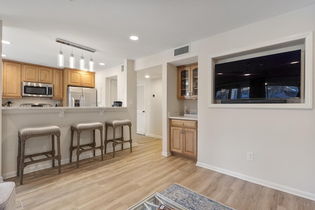 kitchen featuring appliances with stainless steel finishes, a breakfast bar, decorative light fixtures, backsplash, and light wood-type flooring