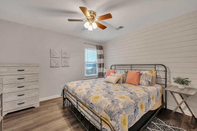 bedroom with ceiling fan, dark hardwood / wood-style flooring, and wood walls