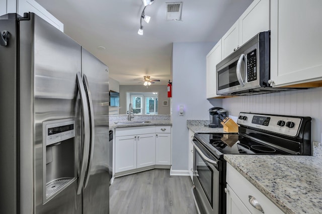 kitchen with stainless steel appliances, white cabinetry, sink, and light stone counters