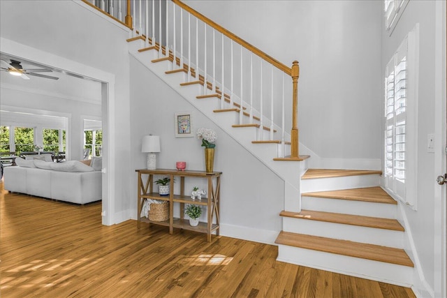 stairway with ceiling fan, wood-type flooring, crown molding, and a towering ceiling