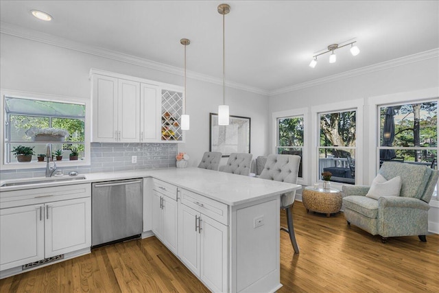 kitchen featuring kitchen peninsula, light wood-type flooring, decorative light fixtures, dishwasher, and white cabinetry