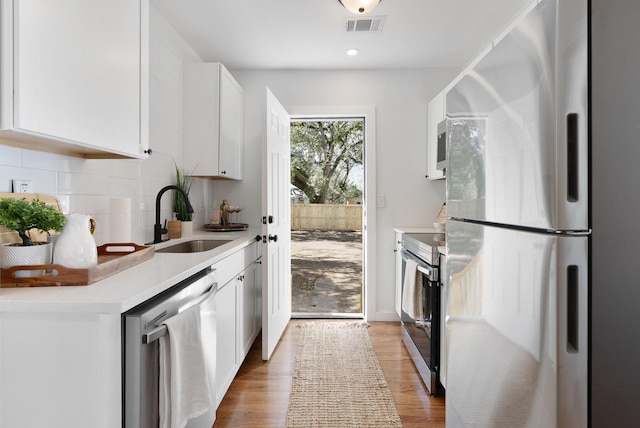 kitchen with visible vents, light wood-style flooring, a sink, tasteful backsplash, and appliances with stainless steel finishes