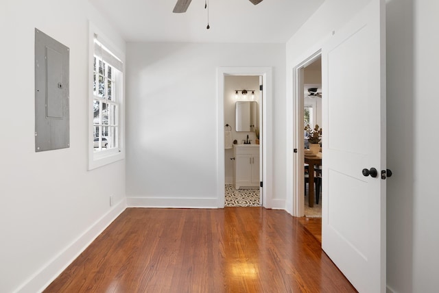 interior space with a ceiling fan, electric panel, a sink, wood finished floors, and baseboards