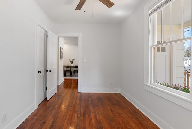 unfurnished room with baseboards, ceiling fan, and dark wood-style flooring