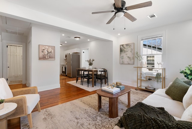 living room featuring visible vents, baseboards, attic access, light wood-type flooring, and recessed lighting