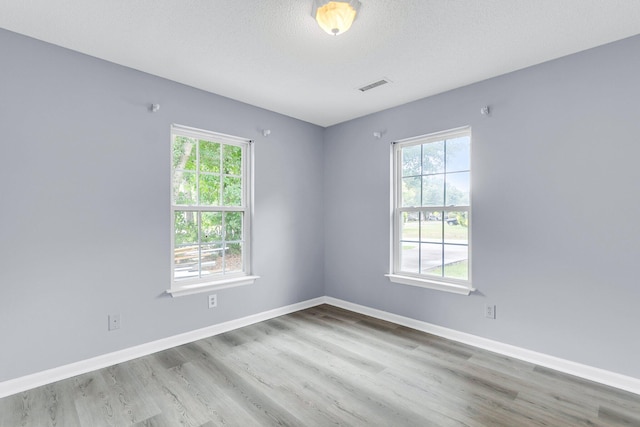 spare room featuring wood finished floors, baseboards, visible vents, and a textured ceiling