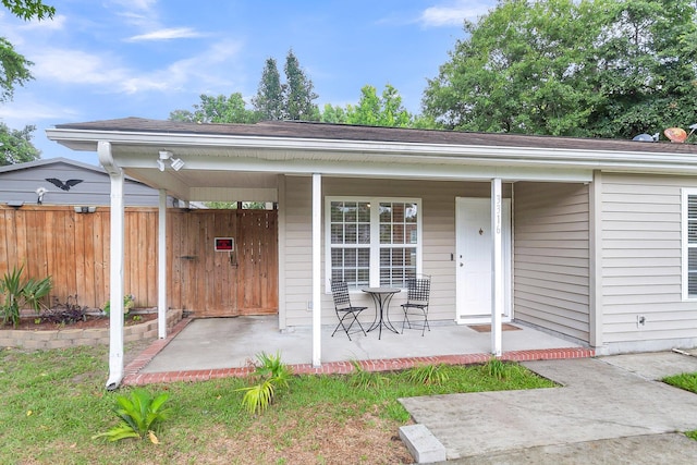 view of exterior entry featuring covered porch and fence