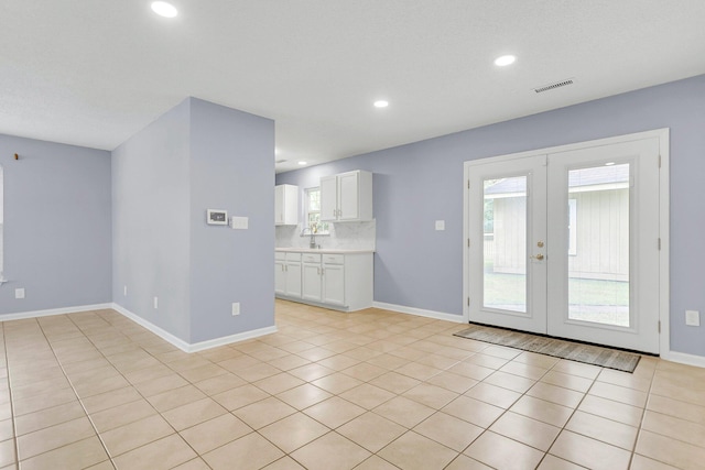 unfurnished living room with a wealth of natural light, french doors, baseboards, and a sink