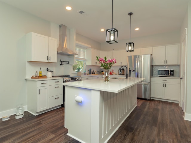 kitchen with a center island with sink, stainless steel appliances, sink, white cabinetry, and wall chimney range hood