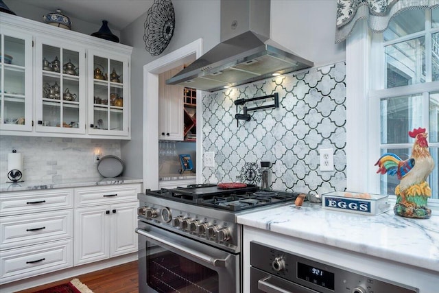 kitchen with high end range, dark wood-type flooring, decorative backsplash, light stone counters, and island exhaust hood