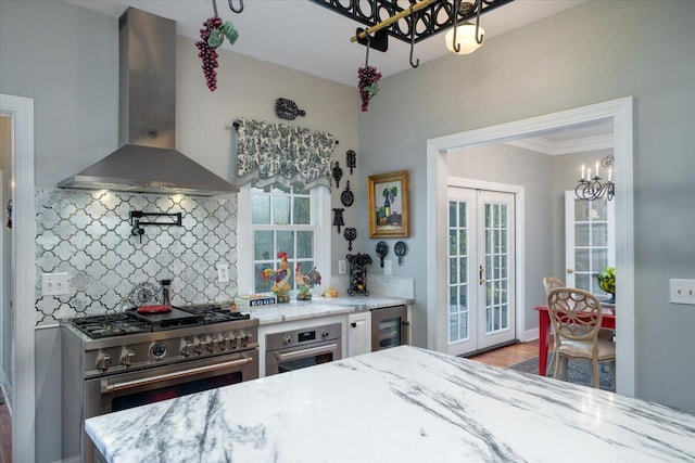 interior space featuring backsplash, stainless steel appliances, hardwood / wood-style floors, french doors, and wall chimney range hood