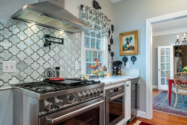 kitchen featuring hardwood / wood-style flooring, light stone counters, tasteful backsplash, stainless steel appliances, and wall chimney range hood