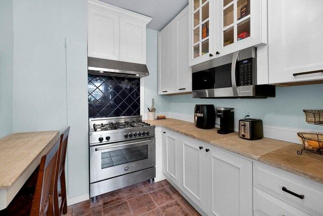 197 Coming St, Charleston, SC 29403 - kitchen with white cabinetry, glass insert cabinets, decorative backsplash, wall chimney range hood, and appliances with stainless steel finishes