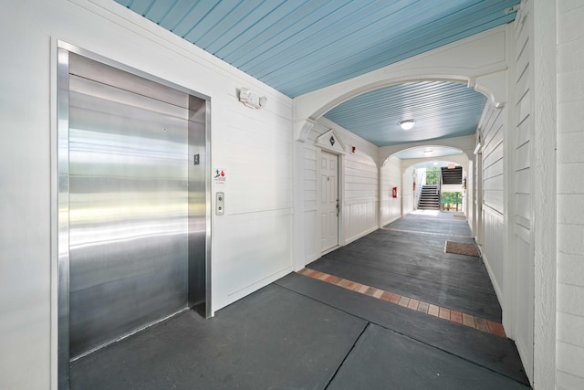 corridor featuring dark hardwood / wood-style flooring, elevator, wooden walls, and wood ceiling