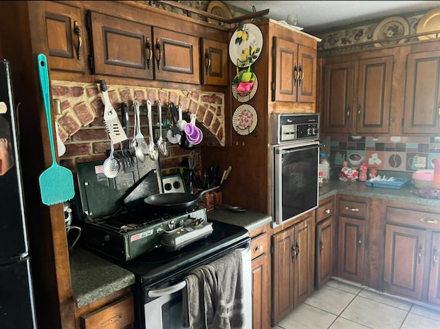 kitchen with tasteful backsplash, light tile patterned floors, stainless steel range with electric stovetop, freestanding refrigerator, and wall oven