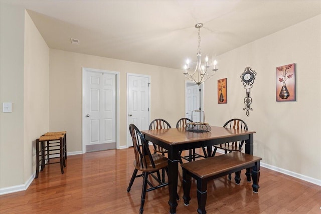 dining area with a chandelier, baseboards, visible vents, and wood finished floors