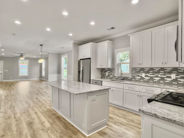 kitchen with ornamental molding, stainless steel refrigerator with ice dispenser, white cabinetry, and a center island