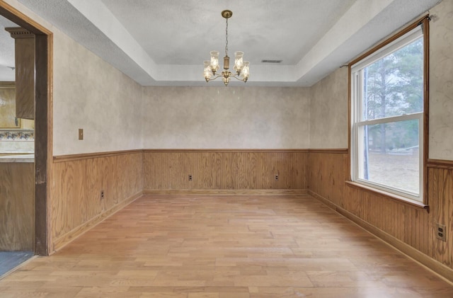 empty room with plenty of natural light, an inviting chandelier, and light hardwood / wood-style flooring